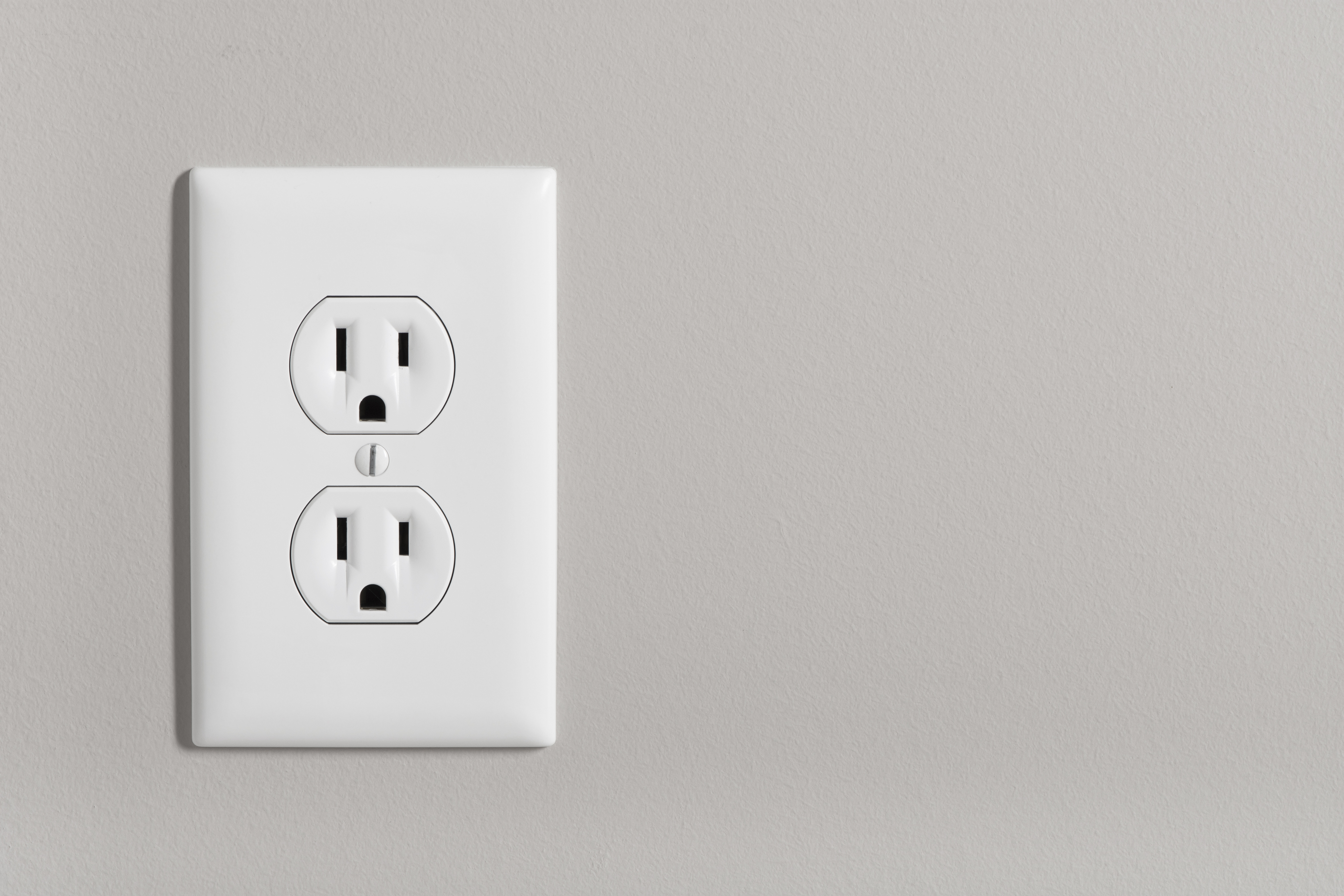 A white home electrical outlet on a light grey wall